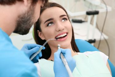Dental hygienist using pick and mirror tools cleaning patient